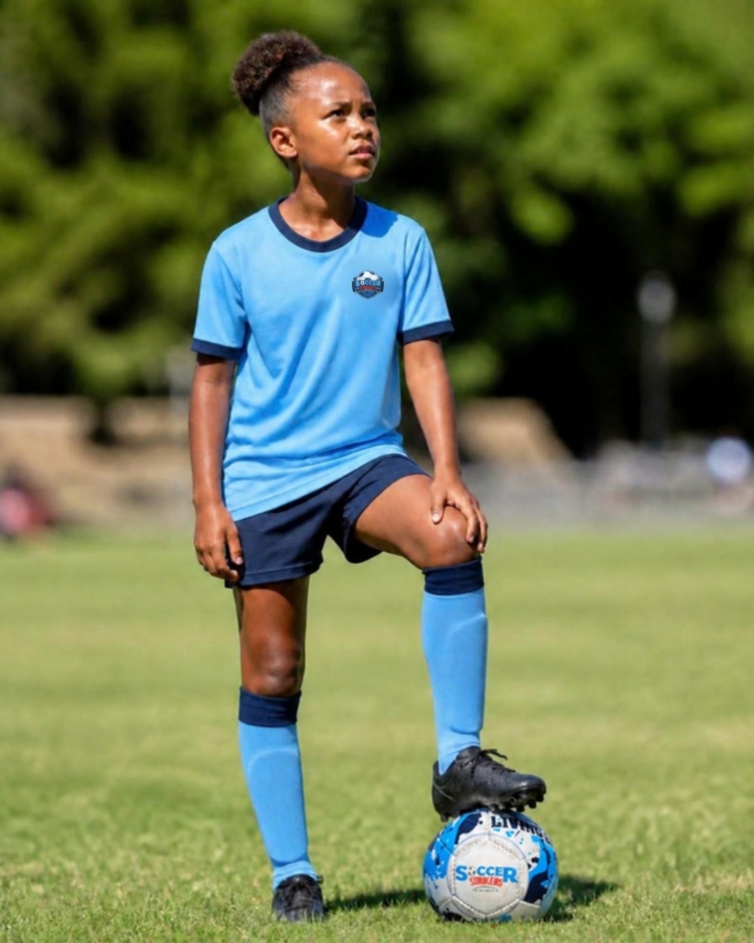 A confident girl in Soccer Strikers kit with her foot on the ball
